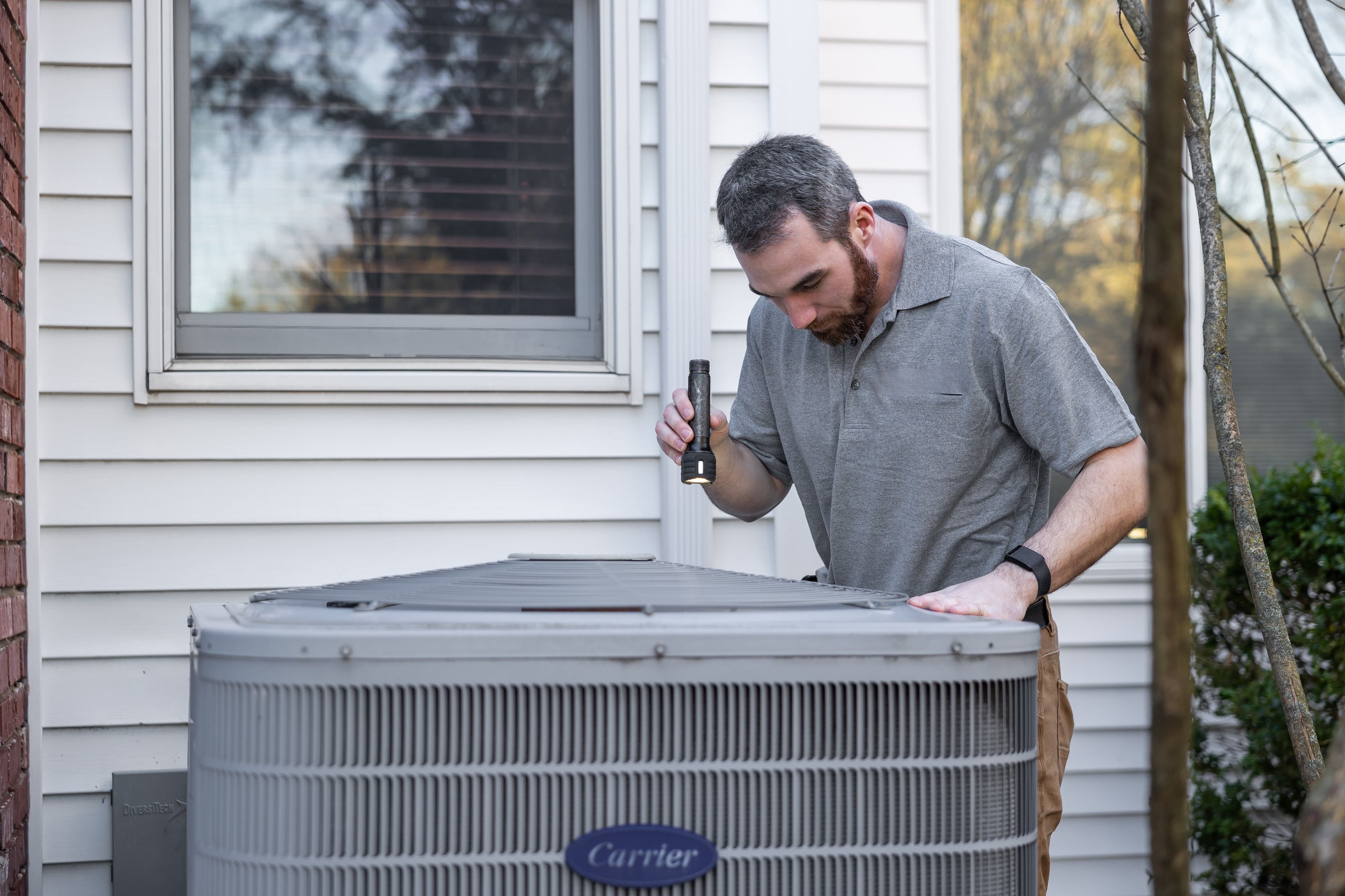 HVAC technician using a tablet beside an air conditioning unit after a completed job