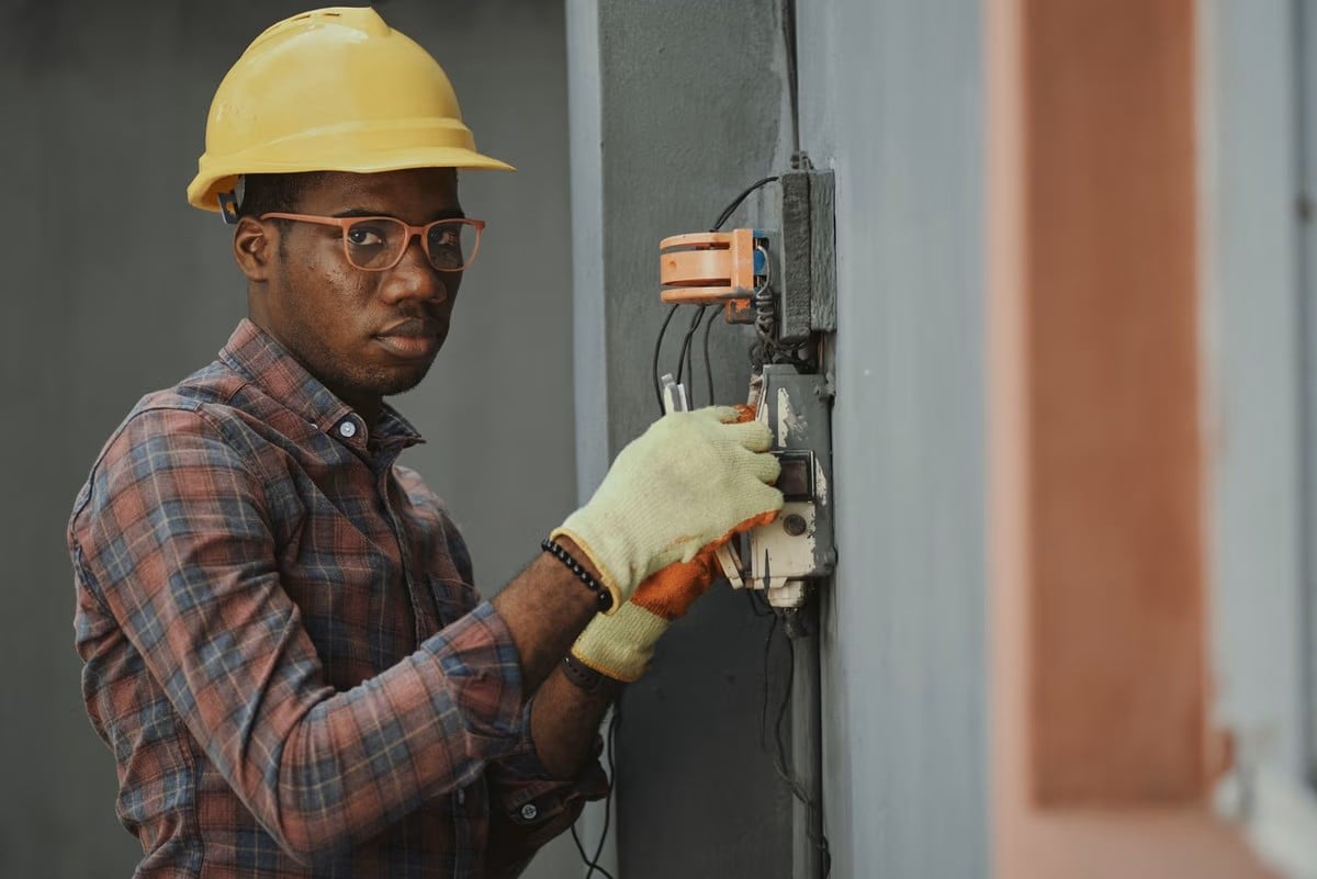 Professional electrician in a hard hat and safety glasses servicing an electrical box
