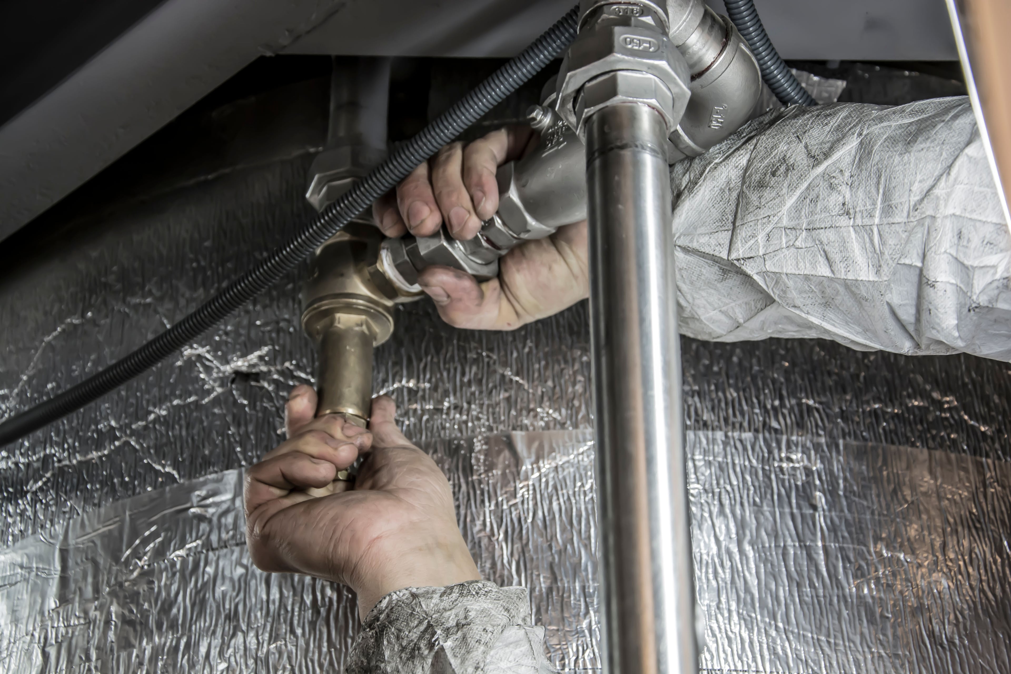 Professional plumber in uniform repairing a pipe during an in-home service call