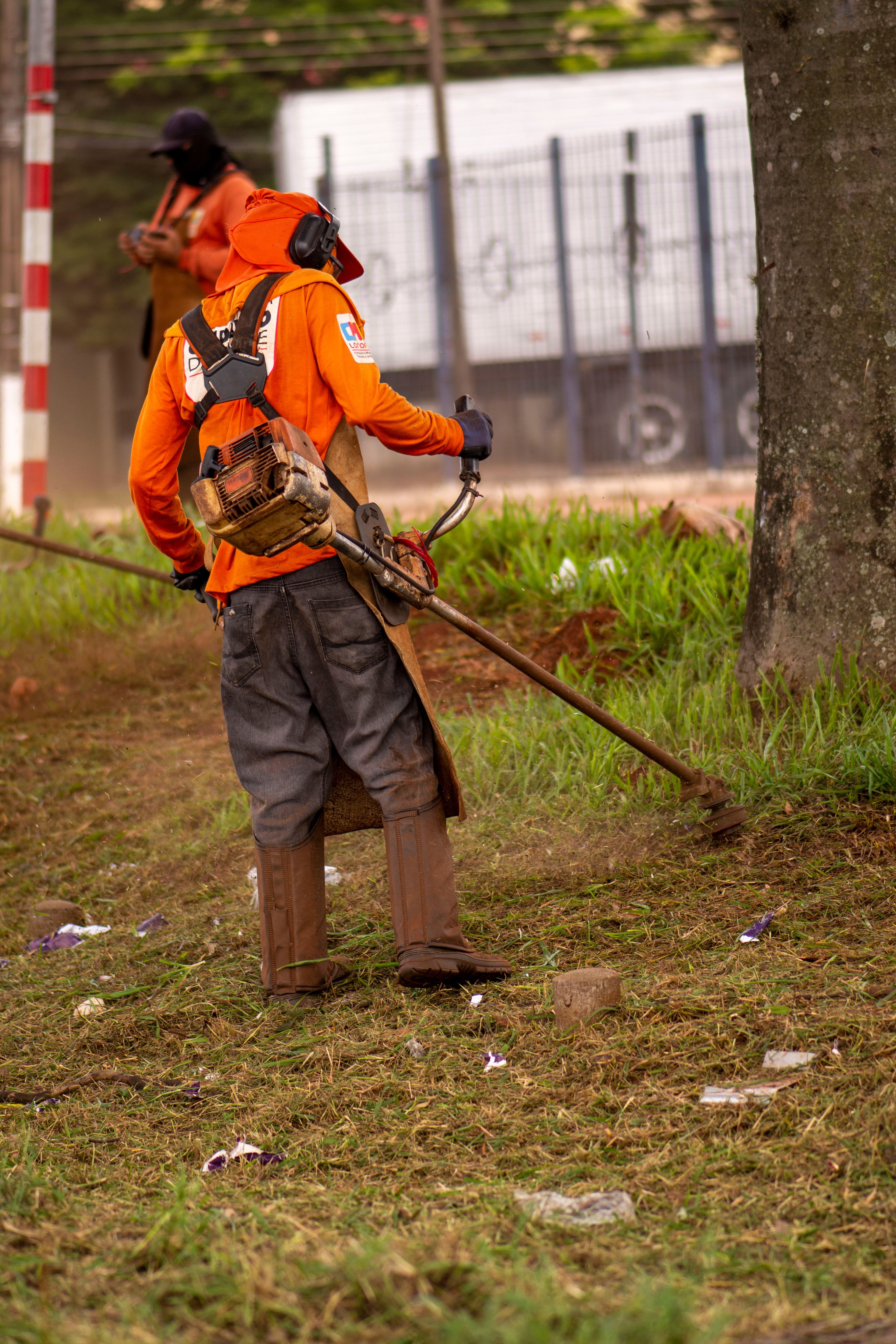 Landscaping crew member in safety gear using a gas-powered string trimmer to edge grass along a property