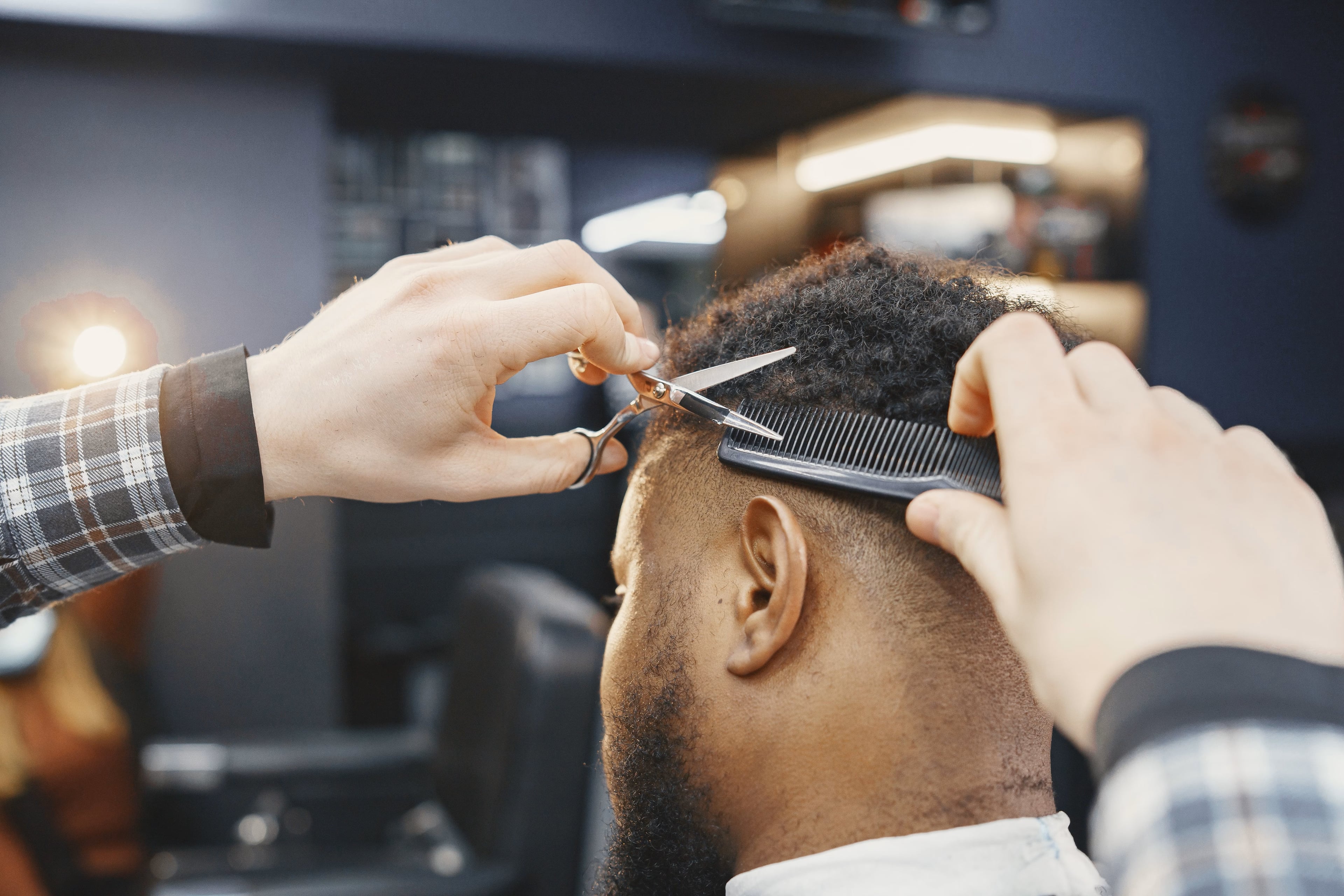 Professional barber giving a client a precise haircut with scissors and comb in a modern barbershop